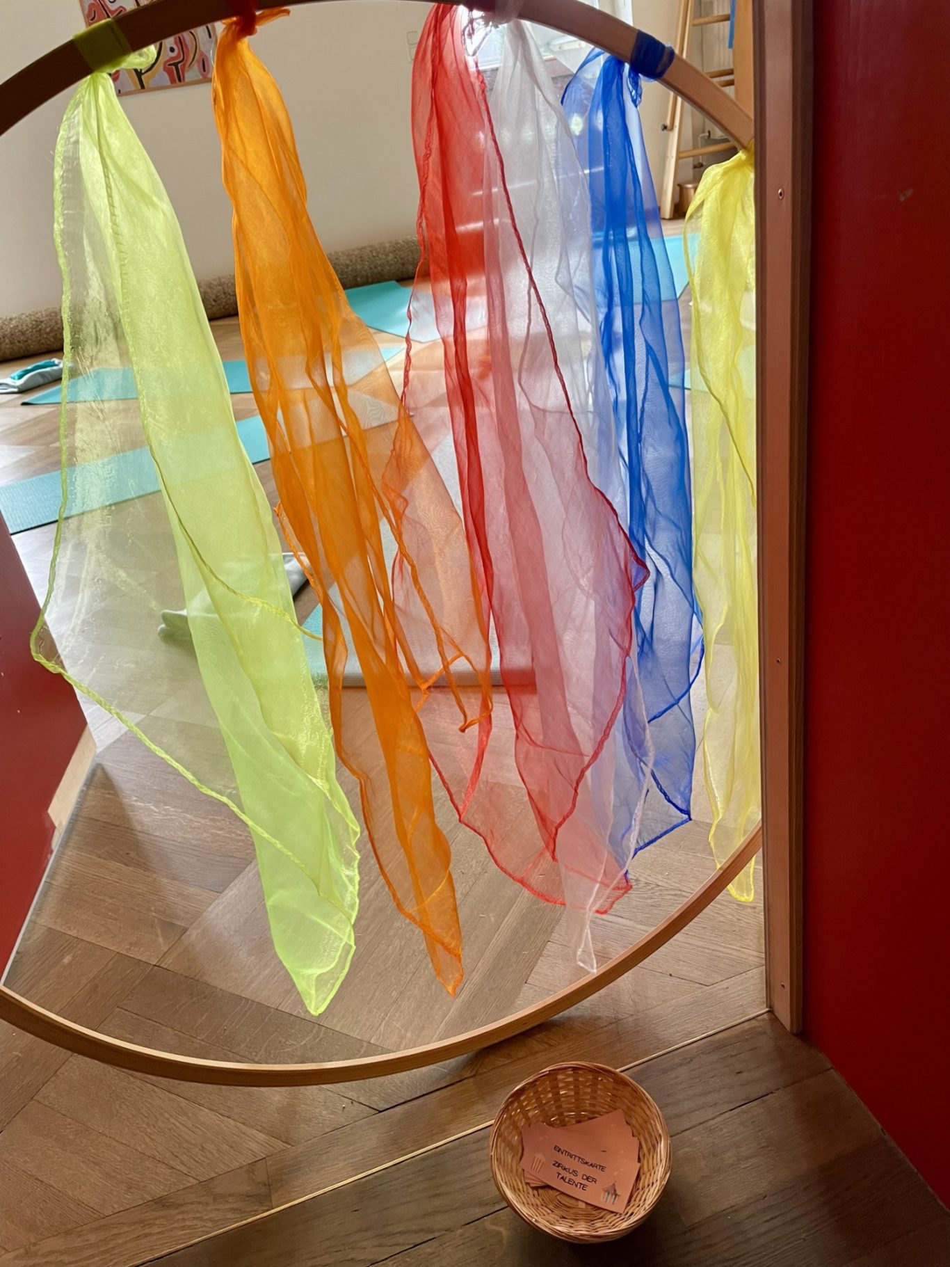 Eingang zum Zirkus der Talente Bunte Schals in verschiedenen Farben hängen an einem Holzring über einem runden Korb.