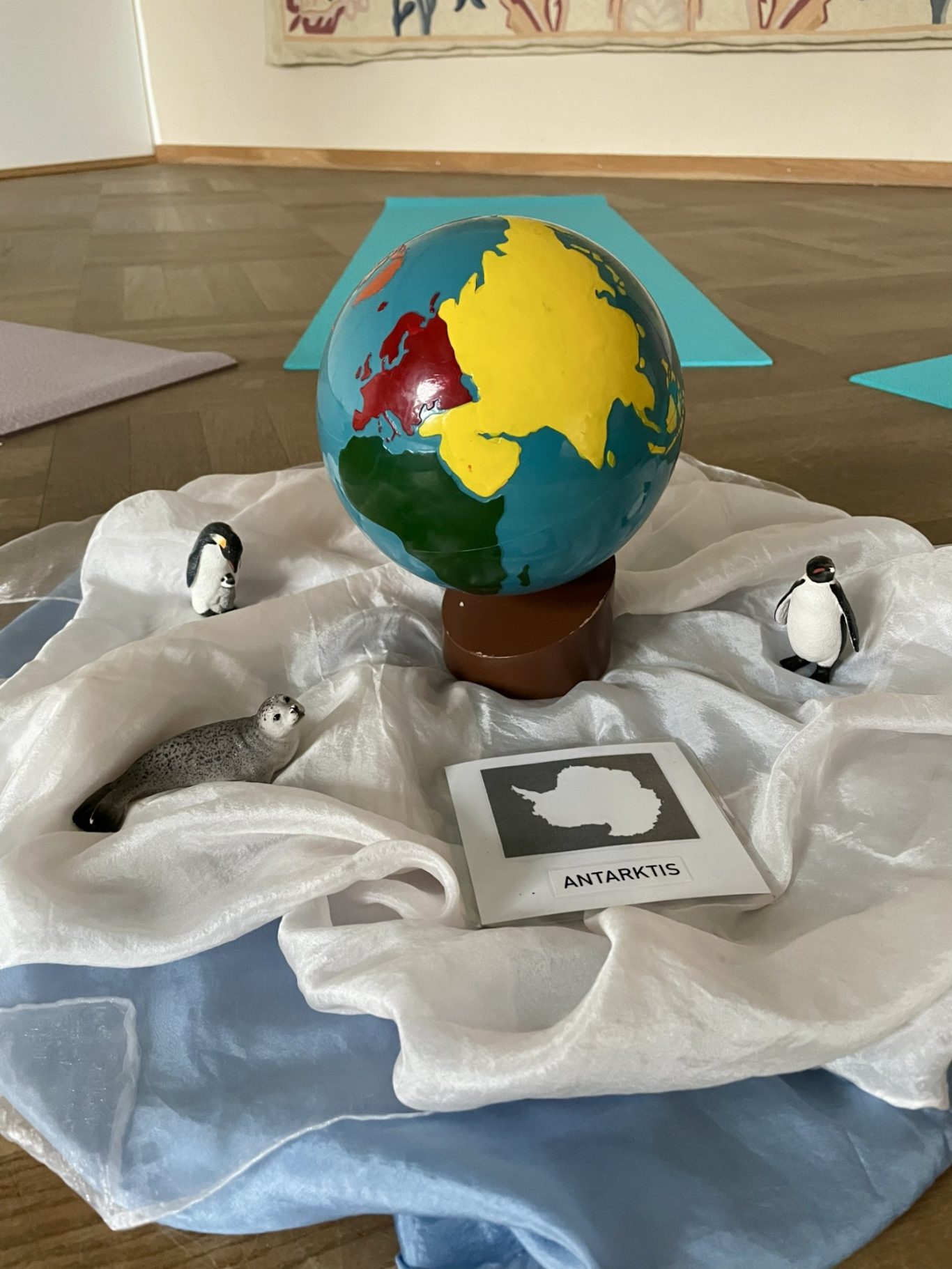 Thema Antarktis mit den Kindergartenkindern Globus mit Kontinenten, umgeben von zwei Pinguinen und einer Karte inmitten von Tüchern.