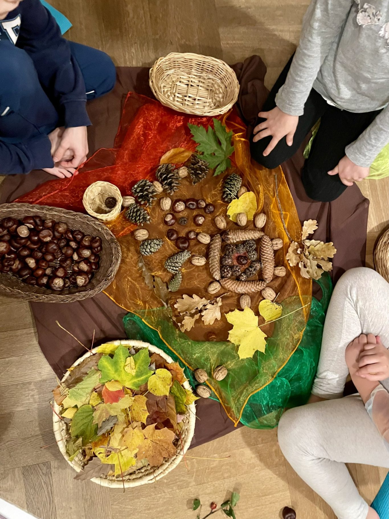 Herbstmandala Mandala aus herbstlichen Materialien wie Blätter, Nüsse und Samen auf einem bunten Tuch ausgebreitet.