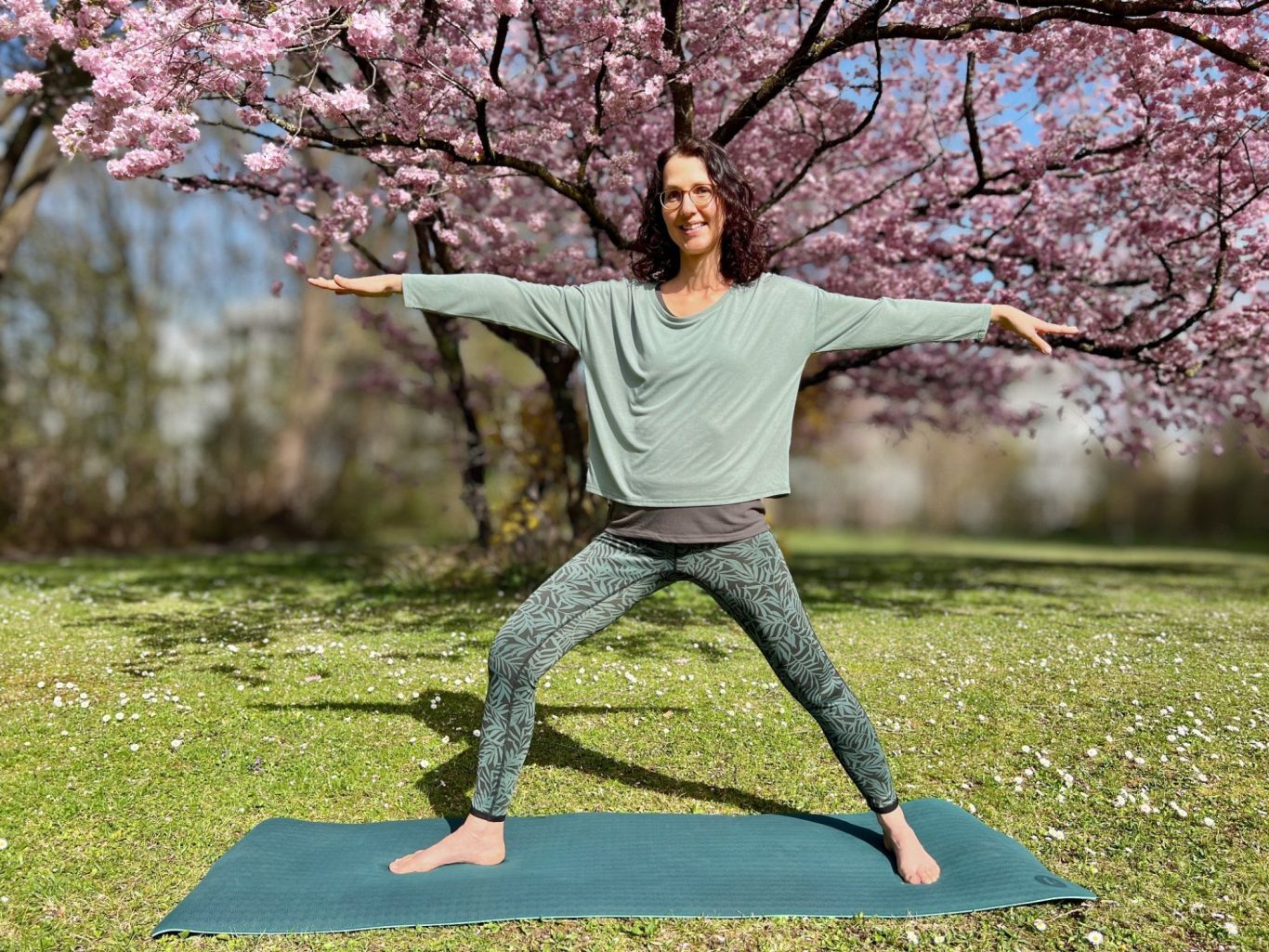 Frau in Yogastellung im Freien, umgeben von Blumen und grünem Gras.