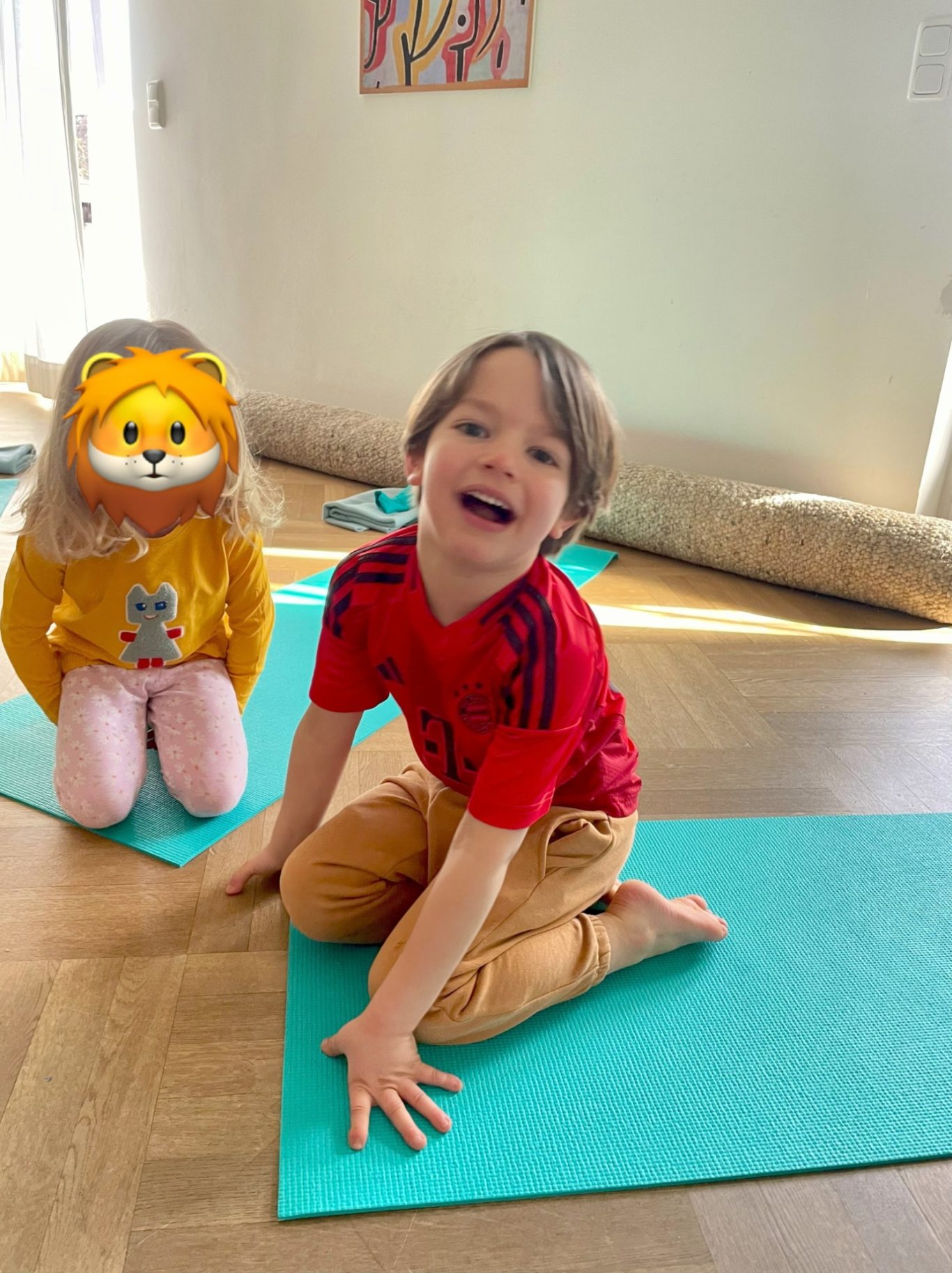 Löwenatmung Ein lächelnder Junge sitzt auf einer Yogamatte, neben ihm eine Puppe mit Löwenkopf.