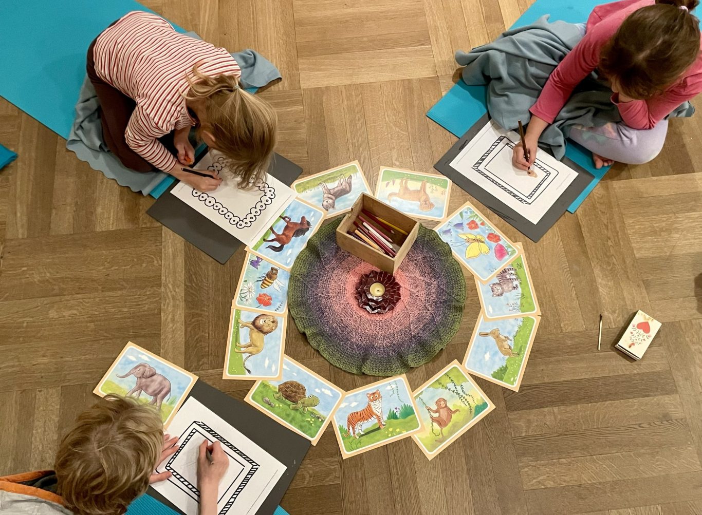 Kinderyoga-Stunde "Mein Krafttier" Drei Kinder sitzen auf dem Boden und zeichnen um eine Kreisformation mit Bilderkarten.