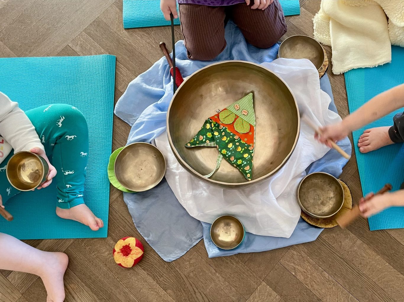 Klangschalen-Spiele Personen sitzen auf Yogamatten, um eine Klangschale mit buntem Muster.