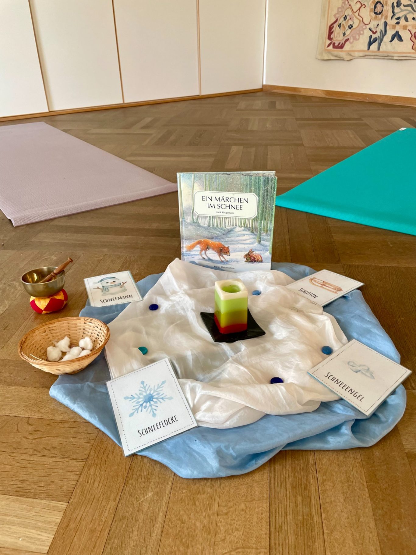 Bilderbuchyoga zum Thema Winter Meditationsraum mit Bücher, Karten und einer bunten Kerze auf einem Tuch.