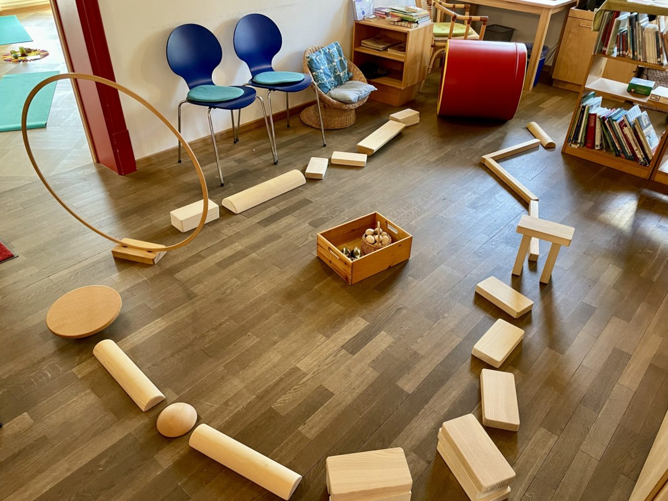 Balancierparcours Holzspielzeug angeordnet in Form eines Herzens im Raum mit Stühlen und Bücherregal.